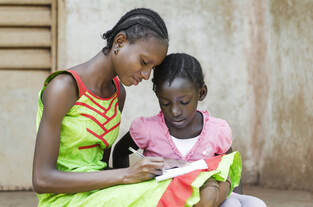 Elder African girl teaching younger African girl