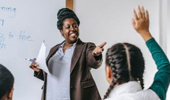 black woman teacher giving word to a student raising hand