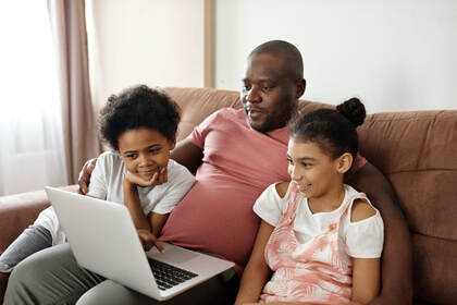 Father sitting on sofa with son and daughter on laptop